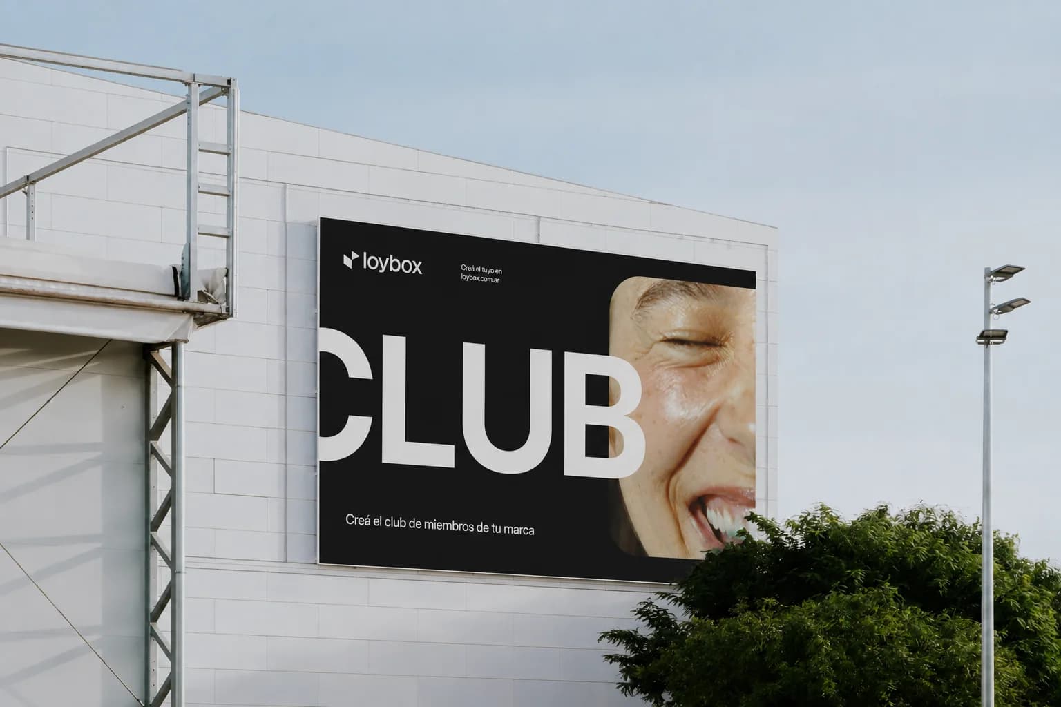 Una cartelera de Loybox en la fachada de un edificio: la palabra CLUB en letras gigantes junto a la foto de una mujer riéndose, y abajo “Creá el club de miembros de tu marca”