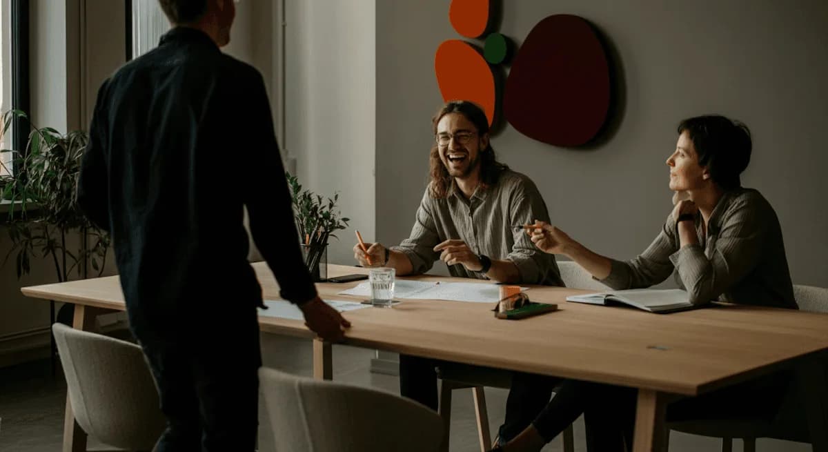 Tres personas conversan de pie alrededor de una mesa larga de reuniones