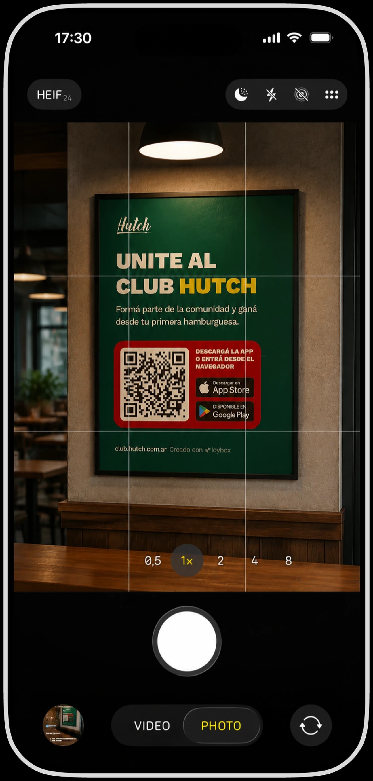 La cámara del iPhone enfocando el cartel del Club Hutch colgado en el local, con el QR y los sellos de las dos tiendas