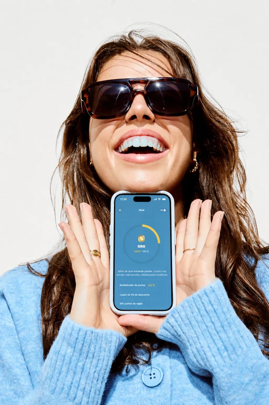 Una miembro riéndose mientras muestra en su teléfono su nivel Oro y los tres beneficios que desbloqueó