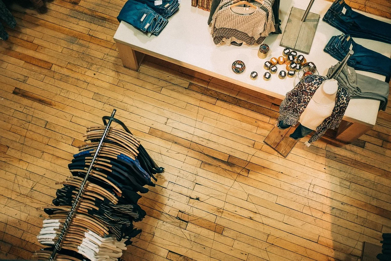 Una tienda vista desde arriba con un perchero de camisas, pantalones doblados y accesorios sobre una mesa de madera