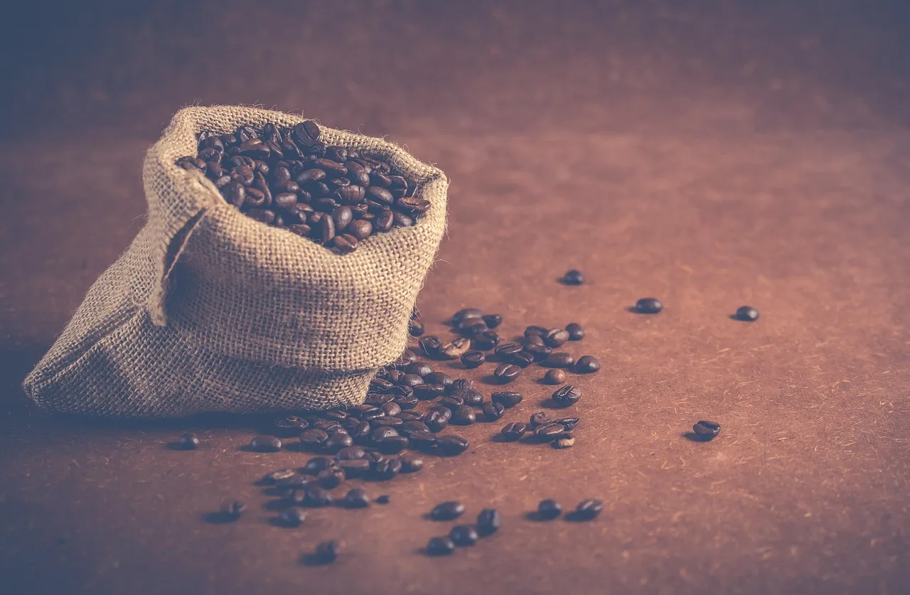 Una bolsa de arpillera abierta llena de granos de café con algunos granos sueltos sobre una mesa