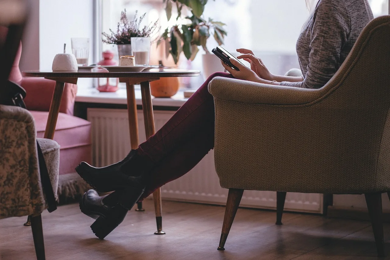 Una persona sentada en un sillón junto a una mesa con plantas revisa su teléfono en un living luminoso