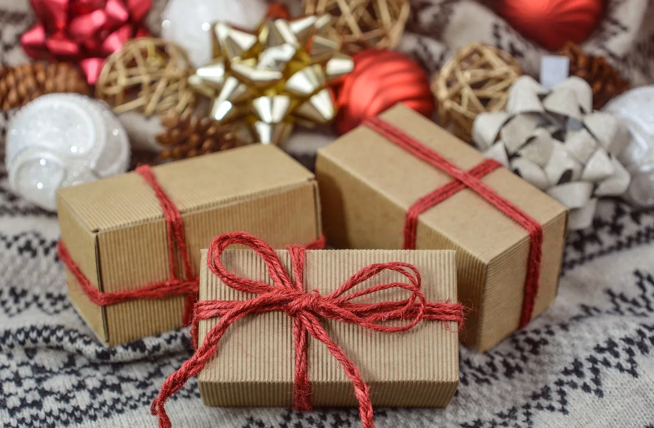 Tres paquetes envueltos en papel madera y atados con hilo rojo entre adornos navideños sobre un tejido