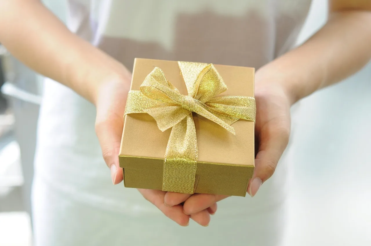 Unas manos sostienen una caja de regalo chica atada con una cinta dorada