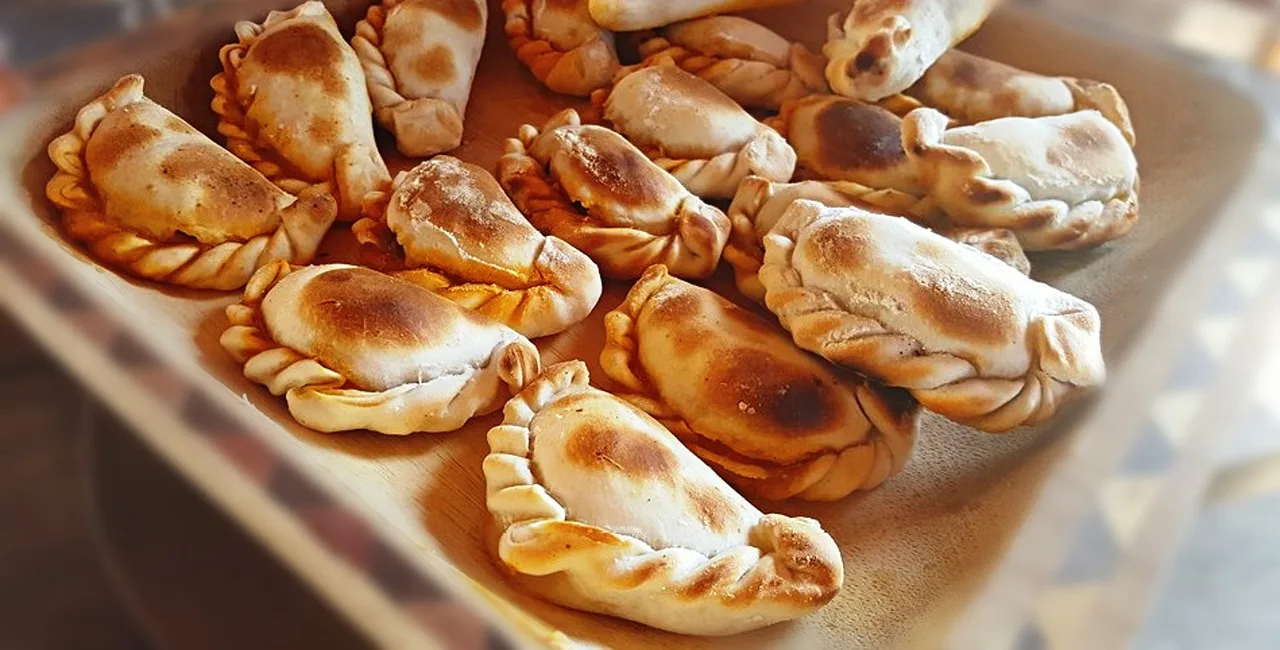 Una bandeja de madera con empanadas horneadas de repulgo dorado acomodadas una al lado de la otra