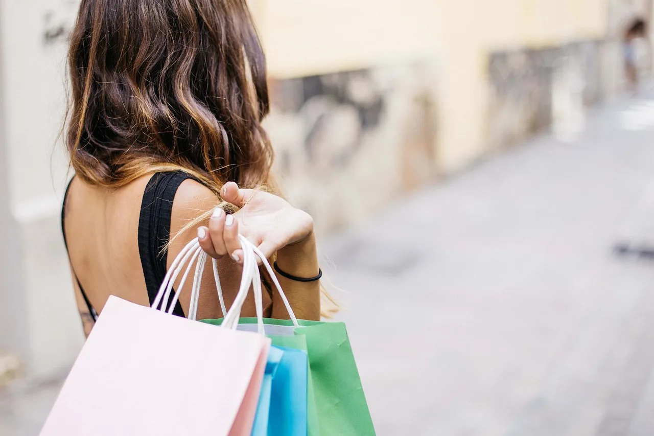 Una mujer de espaldas camina por la calle con varias bolsas de compras de distintos colores en la mano