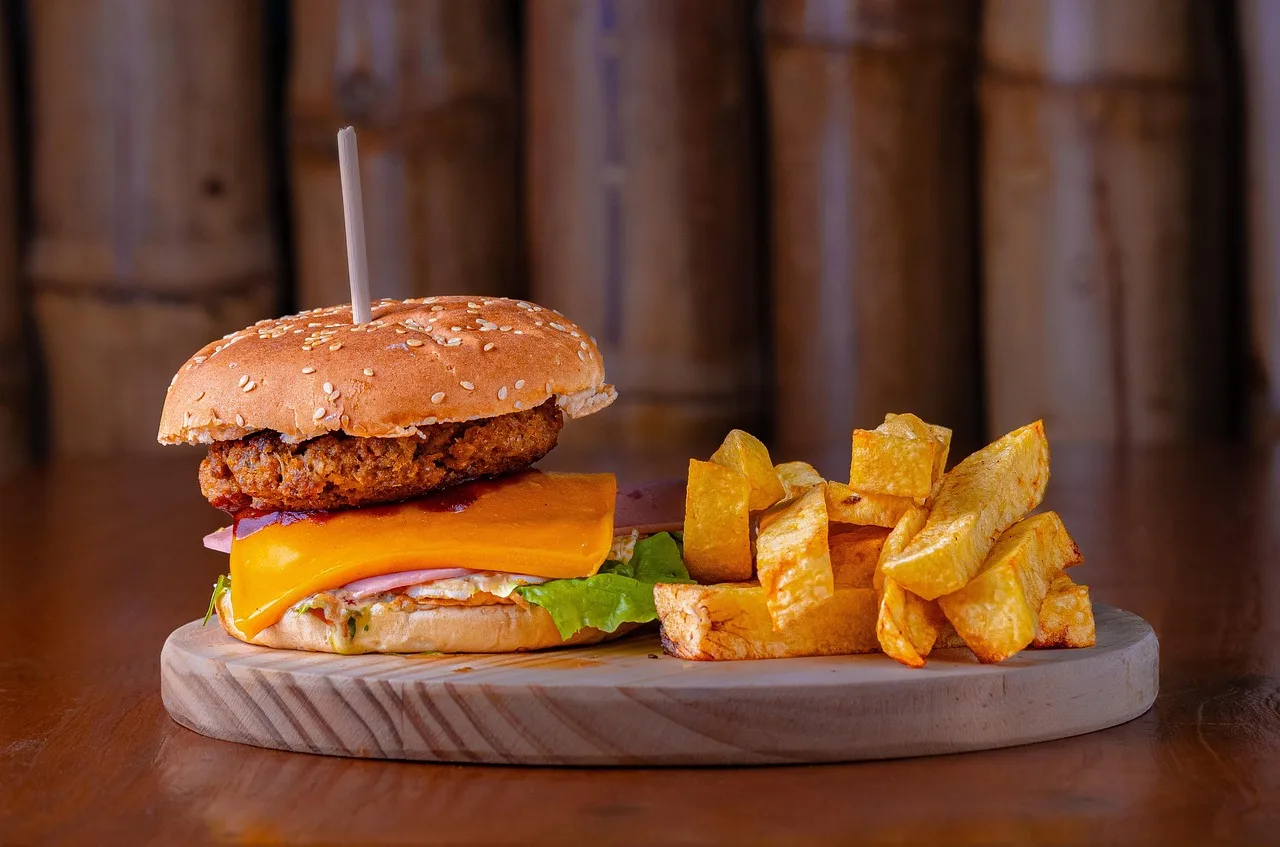 Una hamburguesa con queso y papas fritas servida sobre una tabla de madera en un local de luz cálida