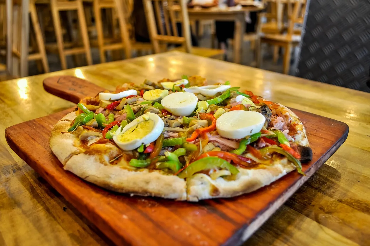 Una pizza con huevo y morrones servida sobre una tabla de madera en el salón de un local